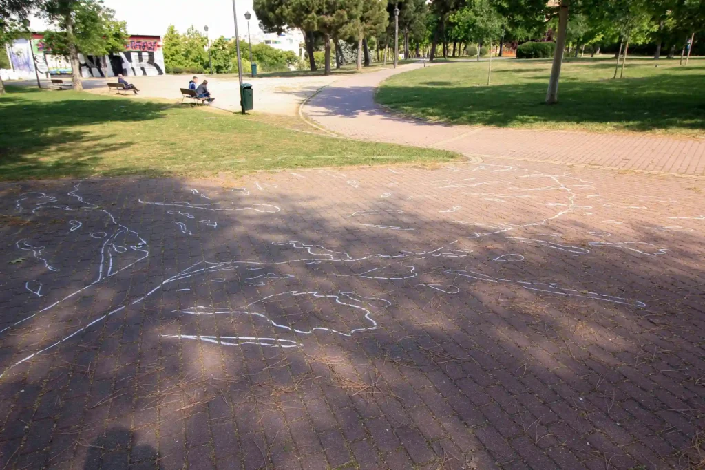 Overhead image showing a white outline on the ground representing where a cut tree should have fallen, merging with a white chalk outline of a victim's body. This artistic installation symbolizes the tragedy of taking a life, with glimpses of park corners visible in the background.