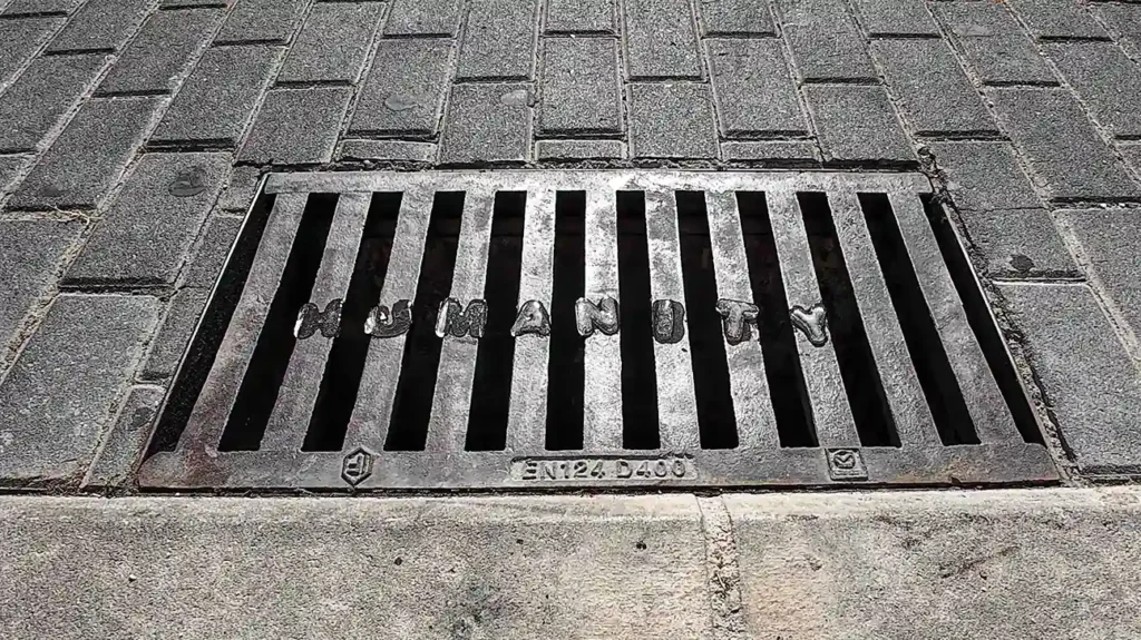 Image of a sewer showing the letters of the word 'HUMANITY' that were placed on it and are created in the ice as it melts between the holes in the sewer.