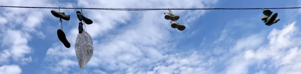 Image taken from below showing wings hanging from electrical cables, along with several pairs of shoes also suspended from the cables.