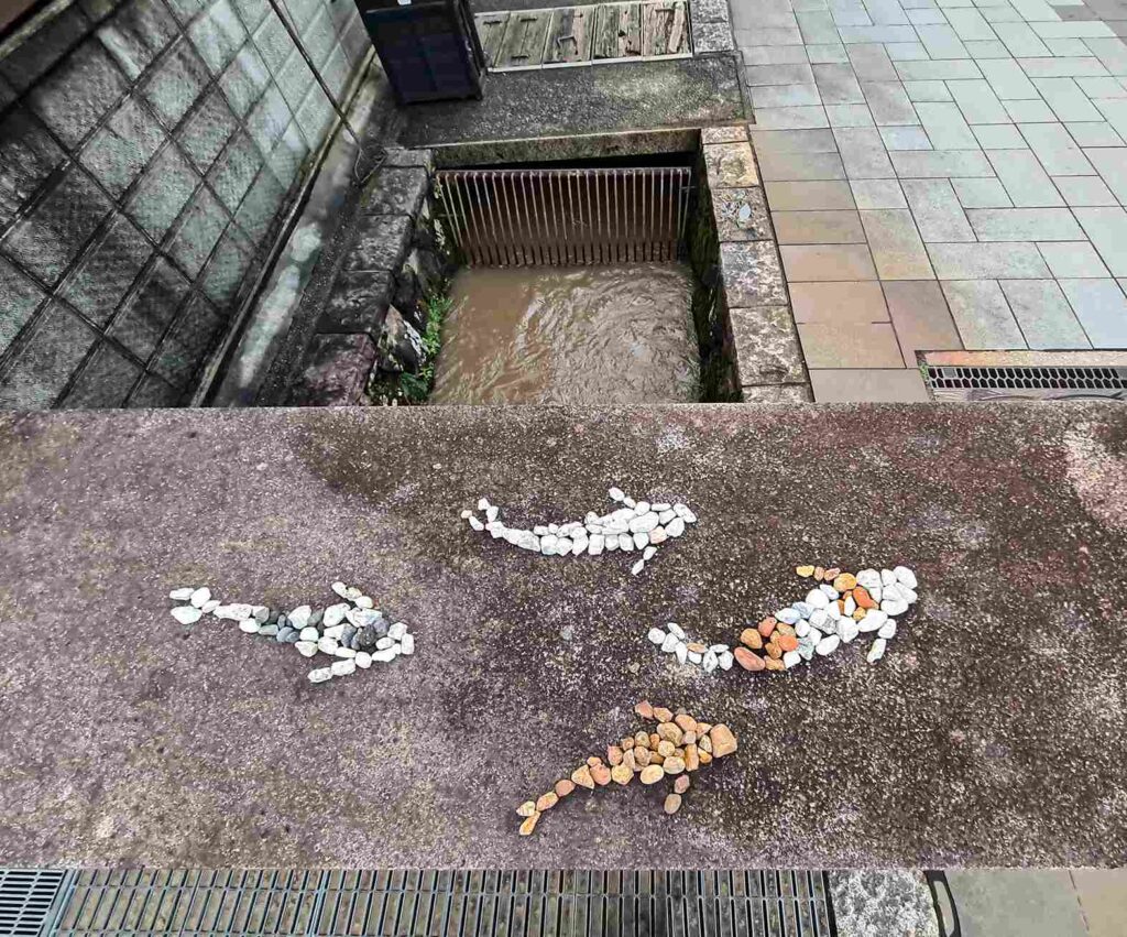 Image of three koi fish created with colored river stones that are placed in the shape of koi fish swimming.