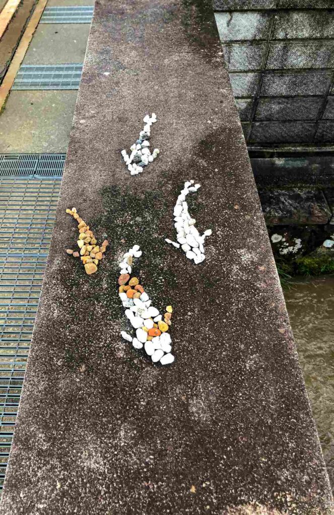 Image of three koi fish created with colored river stones that are placed in the shape of koi fish swimming.