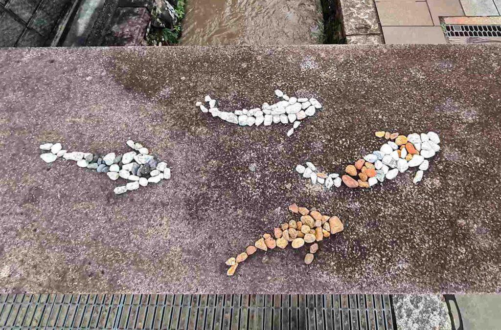 Image of three koi fish created with colored river stones that are placed in the shape of koi fish swimming.