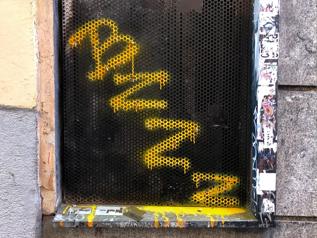 Window screen with the word BZZZ spray-painted in yellow and handcrafted bees made from natural elements